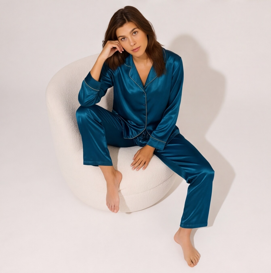 Woman wearing a sapphire blue satin pajama set featuring a long-sleeve button-down shirt with contrast piping and matching full-length satin pants.