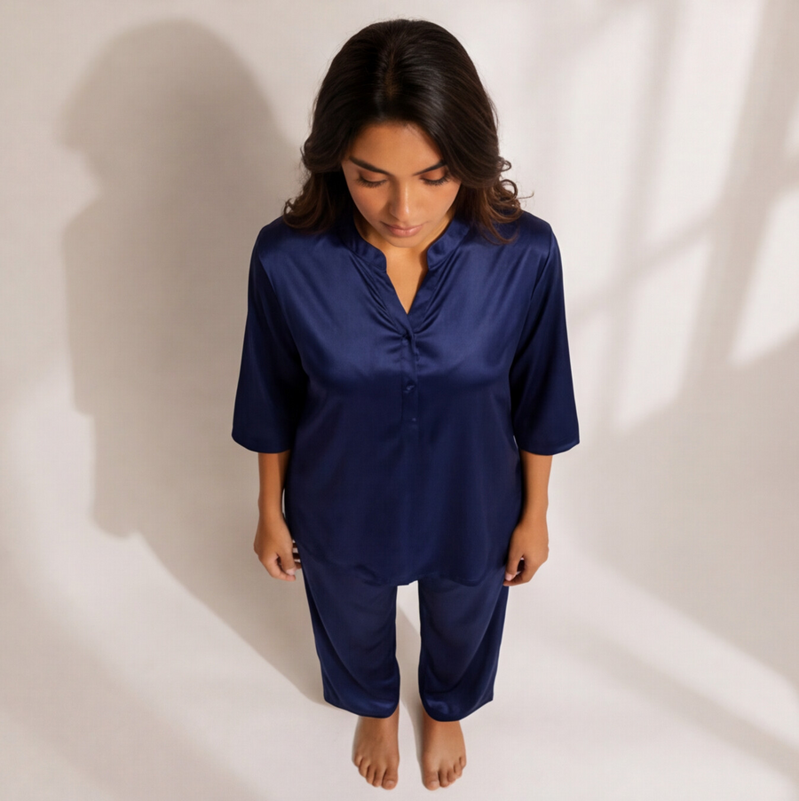 Woman wearing a midnight sapphire blue satin-look lounge set with a split-neck top, three-quarter sleeves, and matching straight-leg pants.