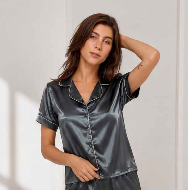 Woman wearing a charcoal grey satin short pajama set featuring a button-down short-sleeve shirt, matching satin shorts, and contrast piping details.