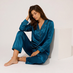 Woman wearing a blue satin pajama set sitting on a white surface.