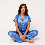 Woman wearing a blue satin pajama set sitting on a white background