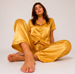Woman wearing a yellow satin pajama set sitting on a white background