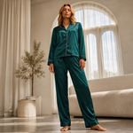 Woman wearing teal satin pajamas standing in a bright room with large windows.