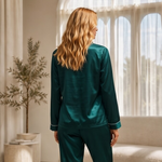 Woman wearing green satin pajamas standing in a bright room with large windows.