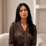 Woman wearing a brown satin pajama top in a softly lit room.