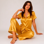 Woman wearing a gold satin pajama set on a plain background