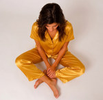 Woman wearing a yellow satin pajama set sitting on a white background